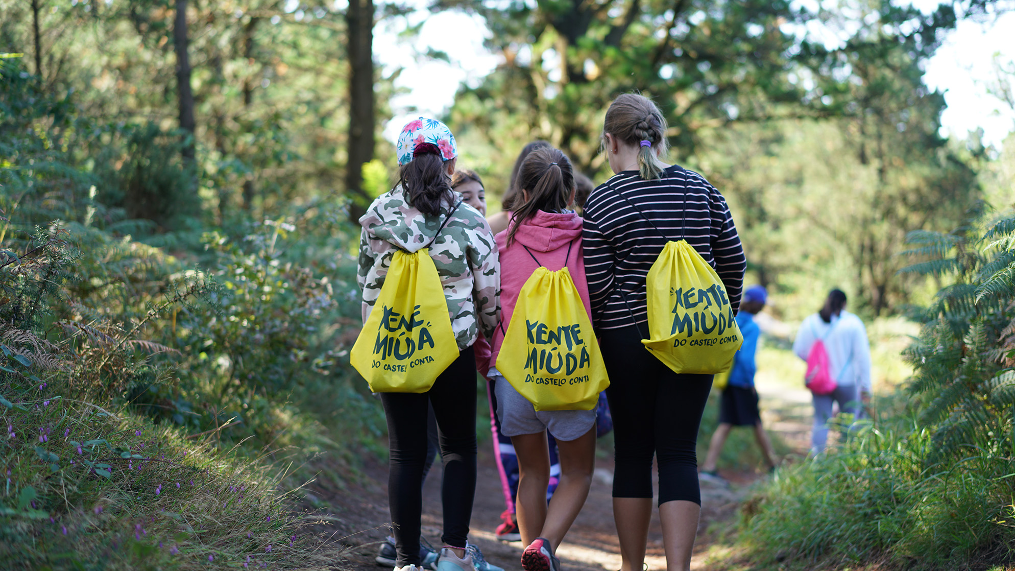 Tres nenas camiñando polo monte Xalo con mochilas rotuladas co logo de Xente Miúda, durante o Castelo Conta do 2019